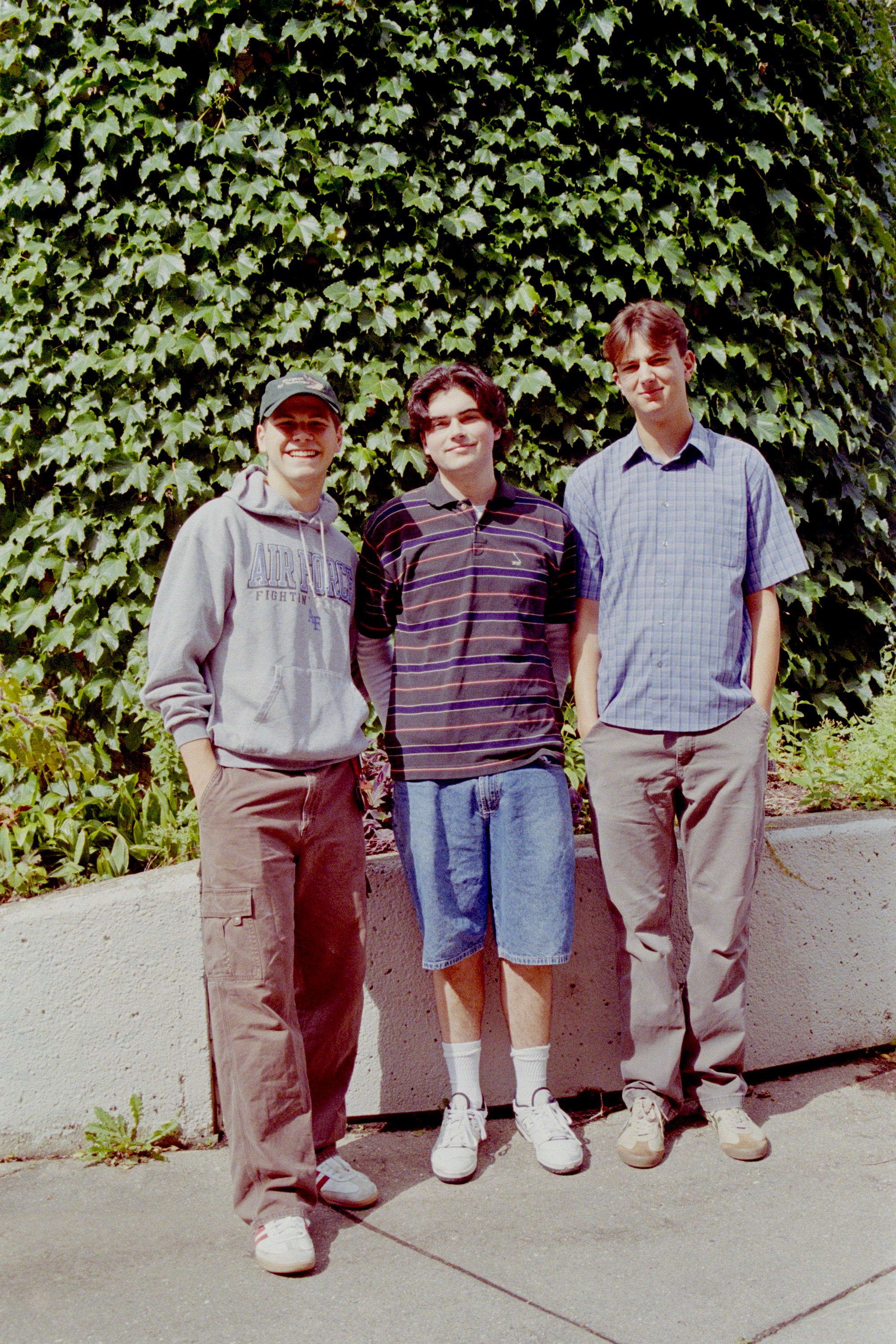 Three men standing in front of a wall of vines